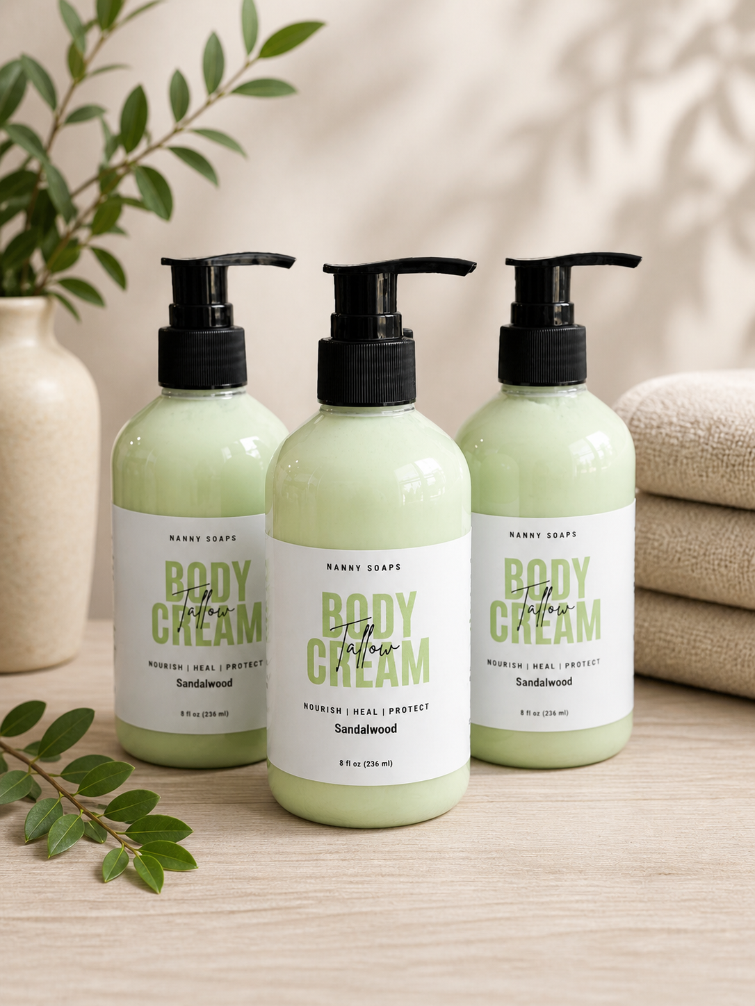 Three bottles of 'Tallow Body Cream' with sandalwood scent on a wooden surface.