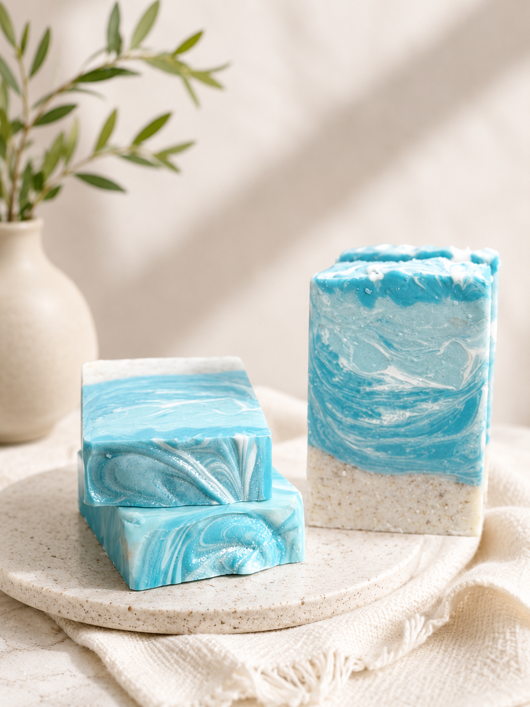 Two bars of blue and white marbled soap on a beige surface with a plant in the background.